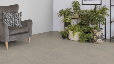 Der Boden im Wohnzimmer ist mit hellgrauem Kork belegt. Es gibt einen bequemen Sessel und einen Ständer mit Grünpflanzen.