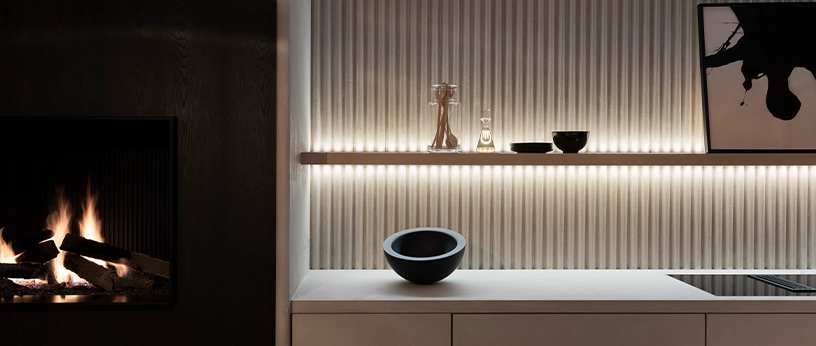 Warme LED-Regalbeleuchtung hebt geriffelte Wand, Dekorobjekte und Kamin in modernem Wohnraum hervor.