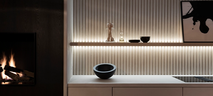 Warme LED-Regalbeleuchtung hebt geriffelte Wand, Dekorobjekte und Kamin in modernem Wohnraum hervor.