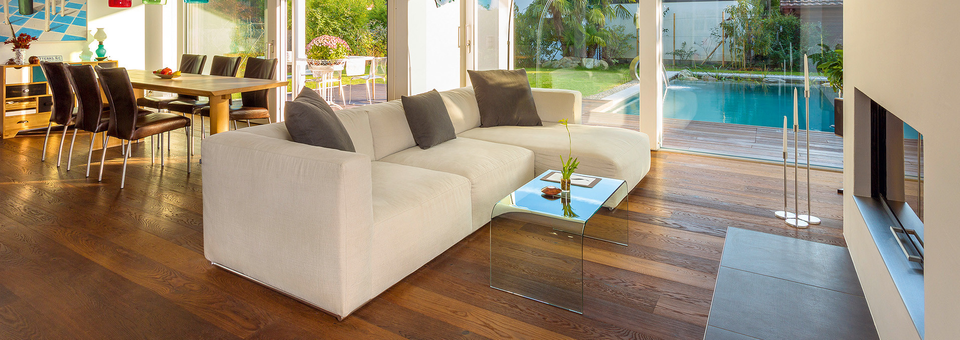 Wohnbereich mit hochwertigen dunklen Massivdielen. Im Hintergrund befindet sich ein von einer Terrasse umgebener Pool