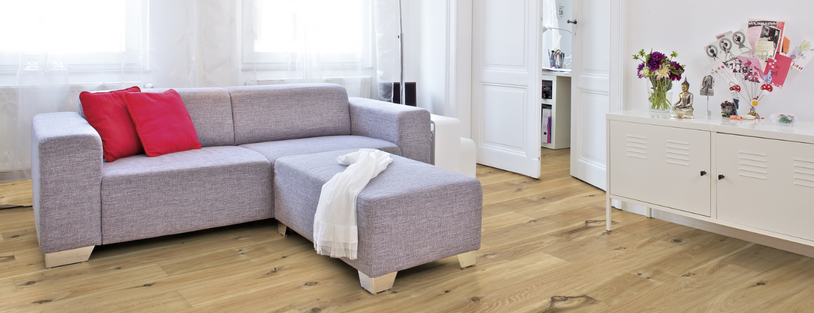 Im Wohnzimmer ist Parkett in Langdielen-Optik verlegt. Dazu passt ein Ecksofa mit bunten Kissen.